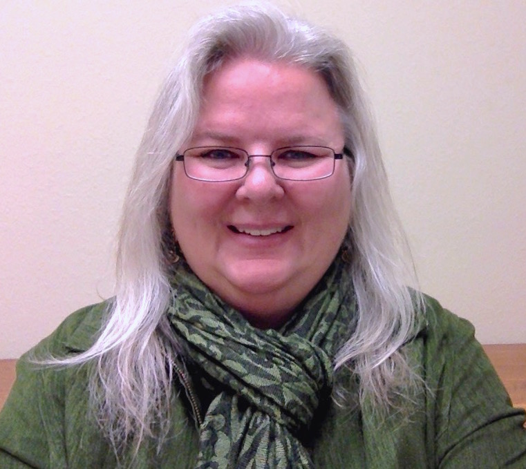 Picture of white woman with glasses and silver hair wearing a green sweater and a green scarf. Christy Albright